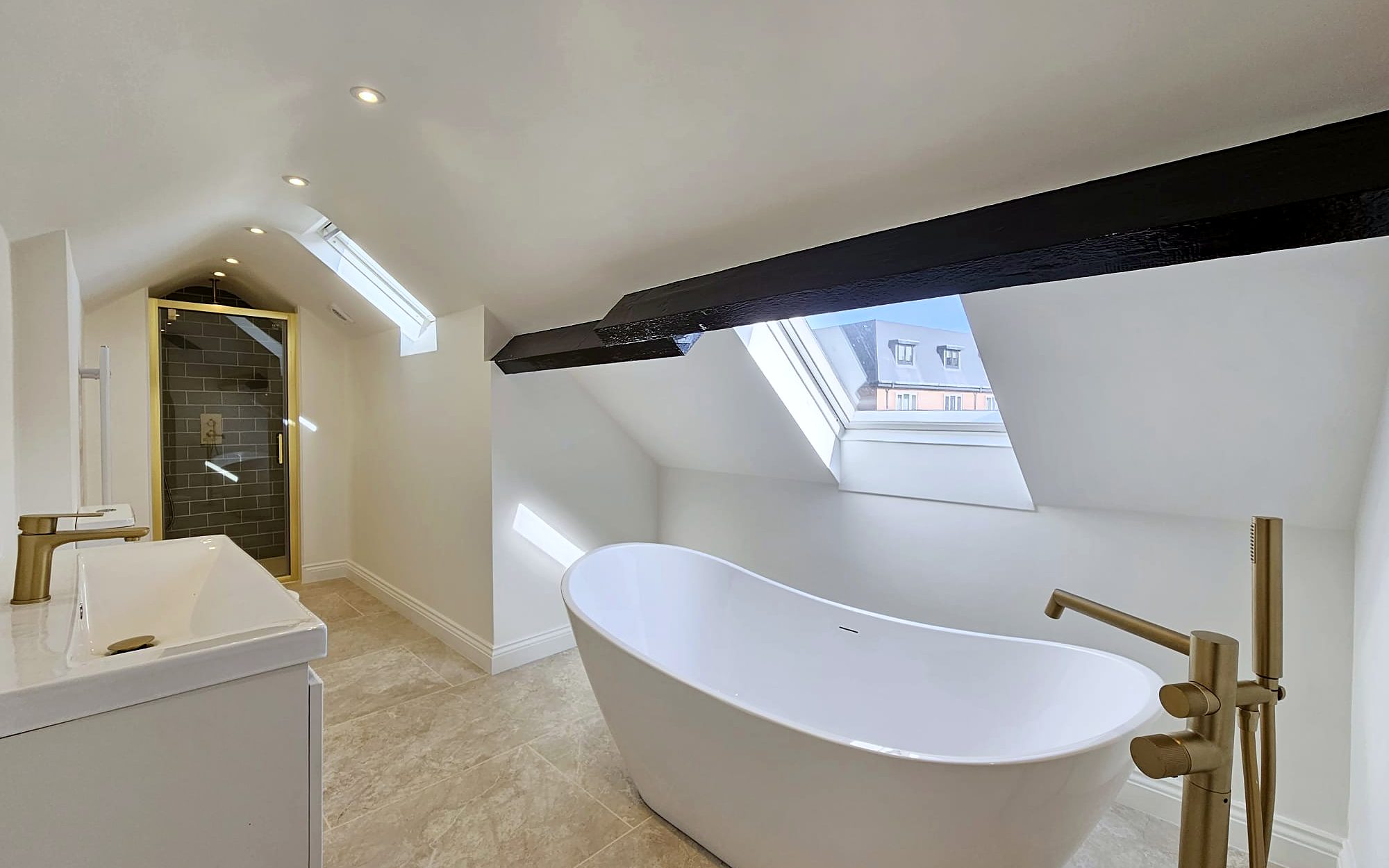 Loft conversion bathroom with freestanding bath, brass taps, exposed beam and skylights