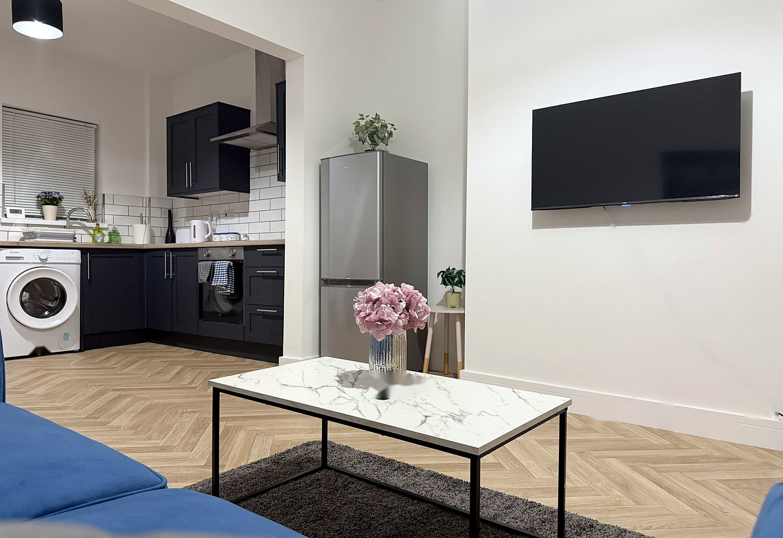 Open-plan lounge with wall-mounted TV opening onto a navy kitchen